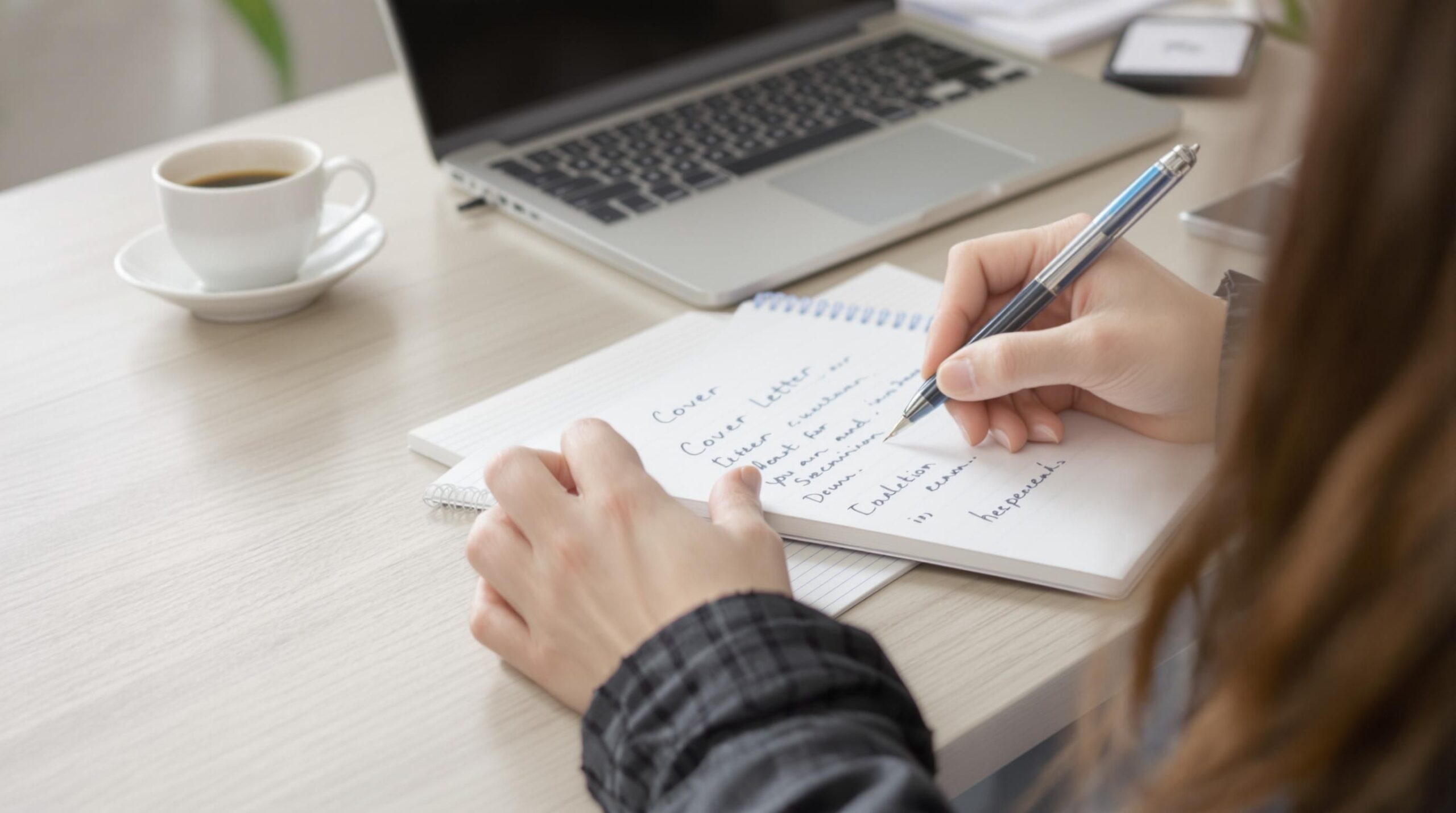 Person writing cover letter at a tidy desk workspace.