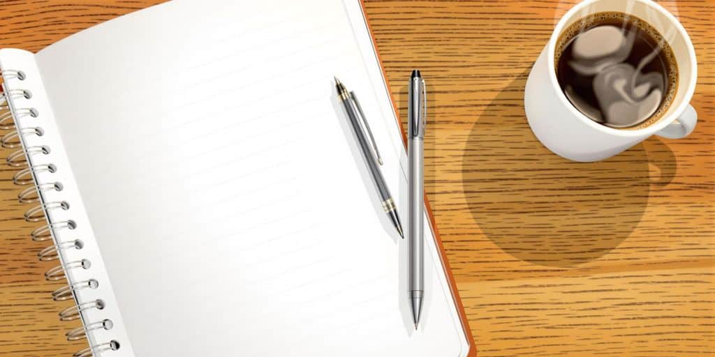 Open notebook, pen, and coffee cup on a wooden desk.